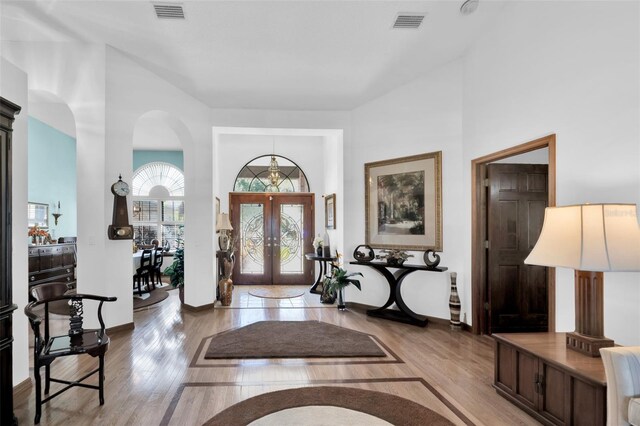 foyer entrance with french doors, light hardwood / wood-style flooring, and a towering ceiling