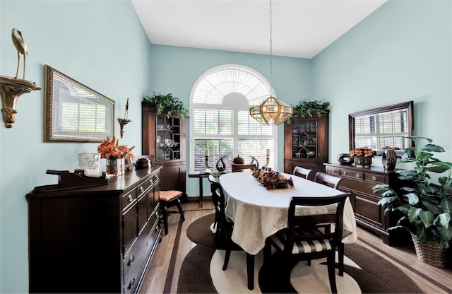 dining area featuring a towering ceiling, an inviting chandelier, light wood-type flooring, and plenty of natural light