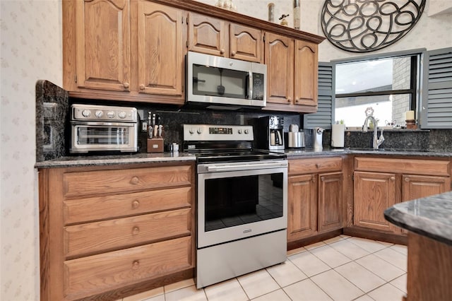 kitchen featuring appliances with stainless steel finishes, decorative backsplash, light tile patterned floors, dark stone counters, and sink