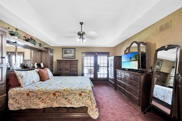 carpeted bedroom with ceiling fan, a tray ceiling, french doors, and multiple windows