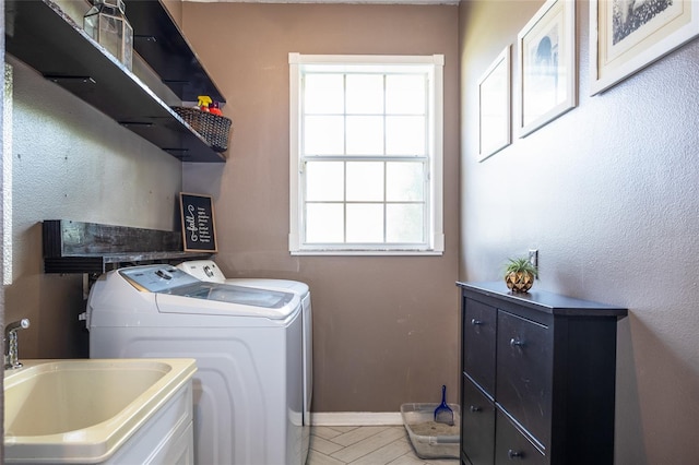 clothes washing area featuring baseboards, separate washer and dryer, a sink, and laundry area