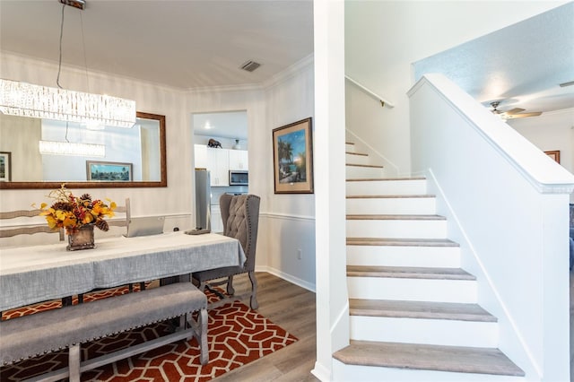 staircase featuring crown molding, wood-type flooring, and ceiling fan with notable chandelier