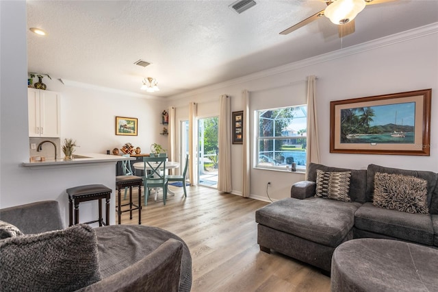 living room featuring light hardwood / wood-style floors, a textured ceiling, ornamental molding, and ceiling fan