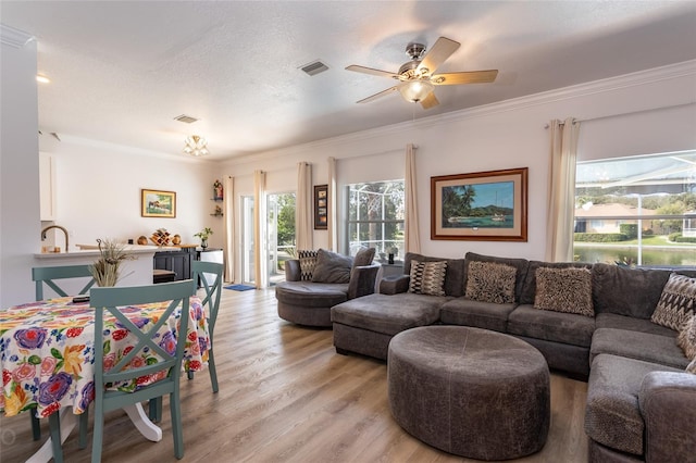 living room with ceiling fan, a textured ceiling, ornamental molding, and light hardwood / wood-style flooring