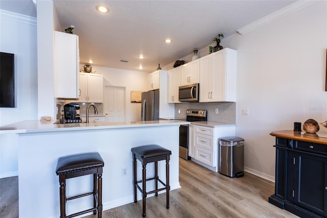 kitchen featuring a kitchen bar, kitchen peninsula, light hardwood / wood-style floors, stainless steel appliances, and white cabinets