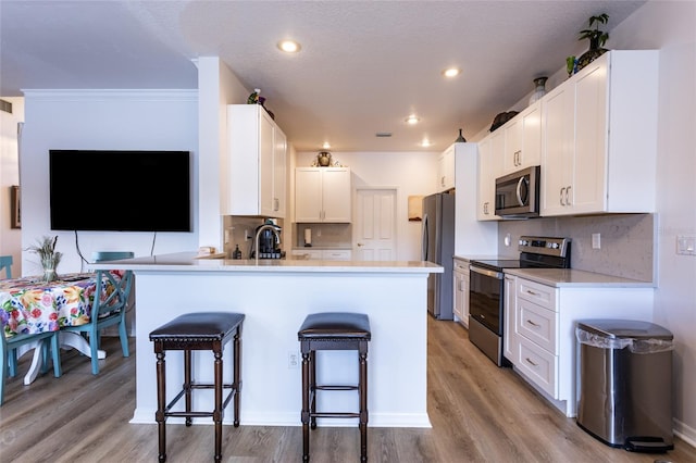 kitchen with kitchen peninsula, a kitchen bar, light wood-type flooring, white cabinetry, and appliances with stainless steel finishes