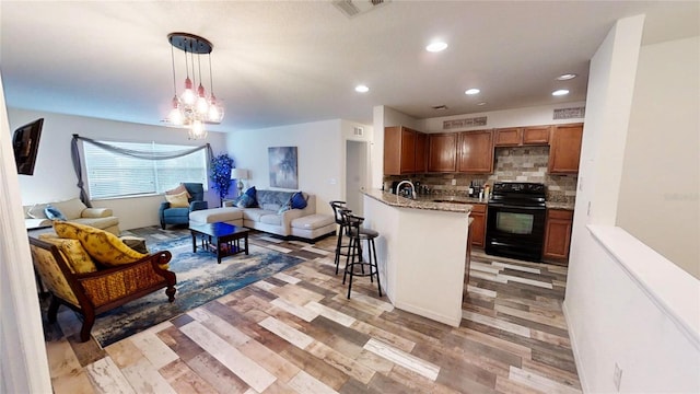 kitchen featuring a kitchen breakfast bar, decorative backsplash, light wood-type flooring, black electric range, and decorative light fixtures