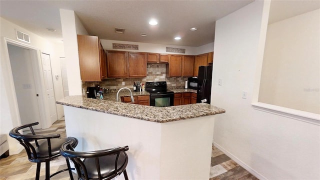 kitchen featuring a breakfast bar, tasteful backsplash, kitchen peninsula, light stone countertops, and black appliances