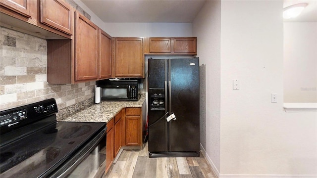 kitchen with light stone countertops, light wood-type flooring, black appliances, and tasteful backsplash