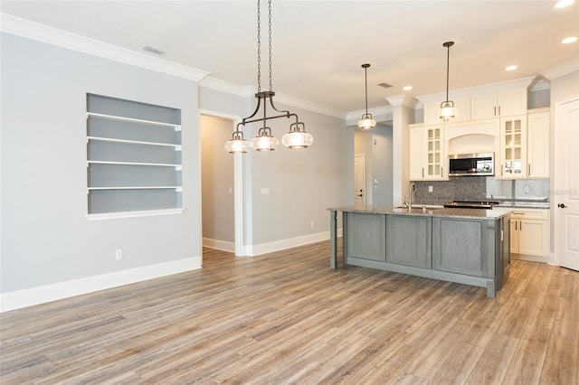 kitchen featuring tasteful backsplash, decorative light fixtures, light hardwood / wood-style floors, and a kitchen island with sink