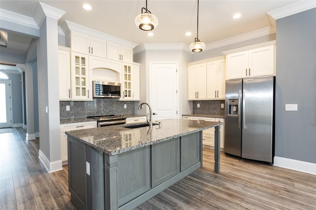 kitchen featuring dark wood-type flooring, a center island with sink, sink, decorative light fixtures, and stainless steel appliances