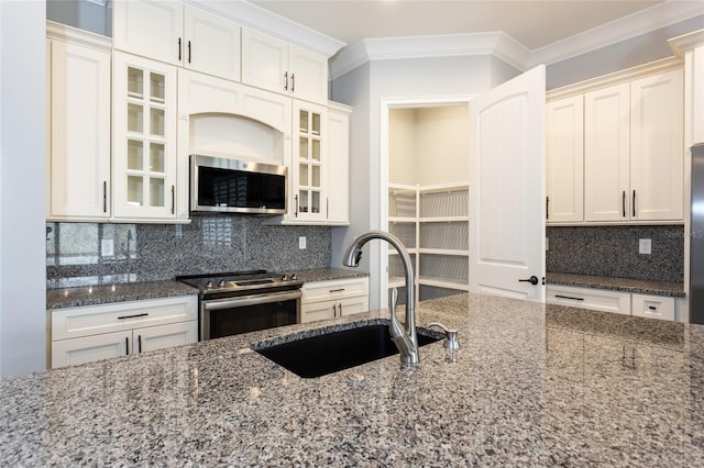 kitchen featuring sink, backsplash, dark stone countertops, crown molding, and appliances with stainless steel finishes