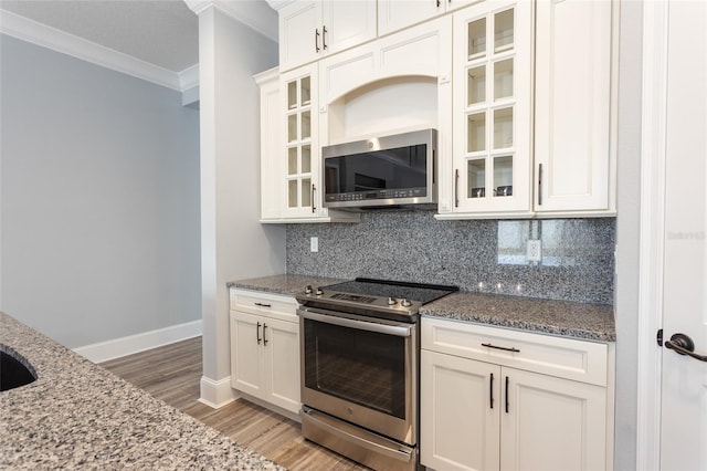 kitchen with light stone counters, ornamental molding, stainless steel appliances, white cabinets, and hardwood / wood-style floors