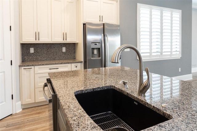 kitchen with light stone countertops, stainless steel refrigerator with ice dispenser, white cabinets, and sink