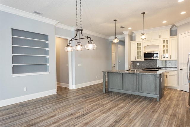 kitchen featuring appliances with stainless steel finishes, tasteful backsplash, dark wood-type flooring, a center island with sink, and decorative light fixtures