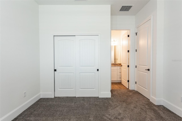 unfurnished bedroom featuring ensuite bathroom, a closet, and dark colored carpet