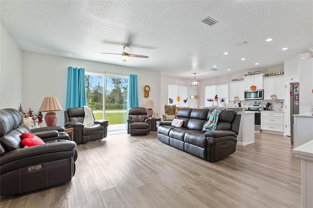 living room with a textured ceiling, ceiling fan, and light hardwood / wood-style flooring