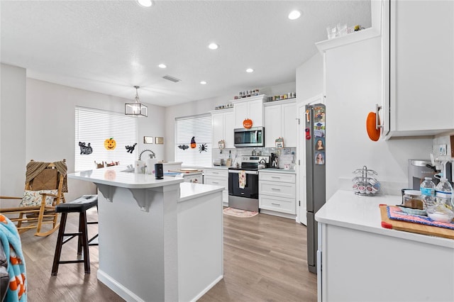 kitchen with pendant lighting, a kitchen bar, white cabinetry, and appliances with stainless steel finishes