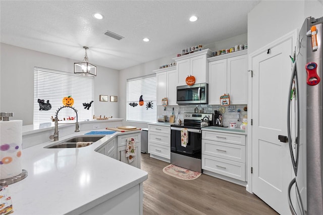 kitchen with a textured ceiling, sink, white cabinetry, hanging light fixtures, and stainless steel appliances