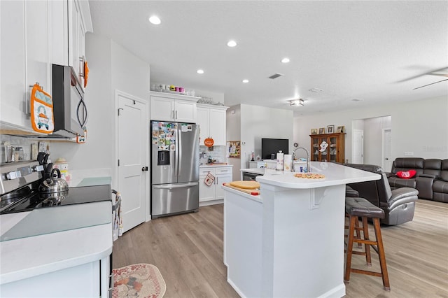 kitchen featuring appliances with stainless steel finishes, white cabinetry, a breakfast bar area, light wood-type flooring, and a center island with sink