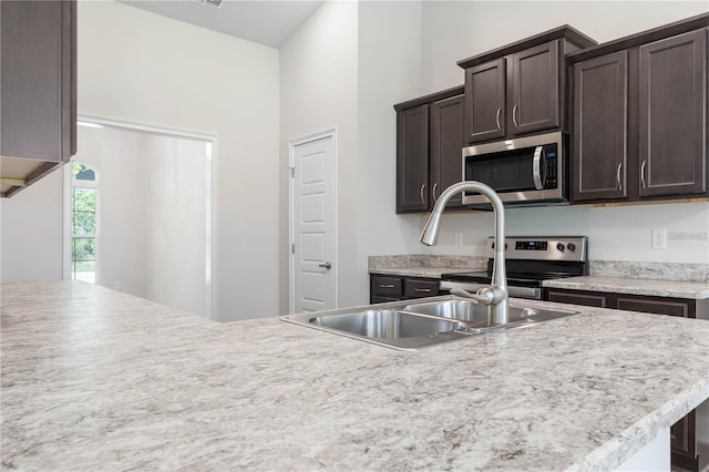 kitchen with dark brown cabinetry, appliances with stainless steel finishes, a towering ceiling, and sink