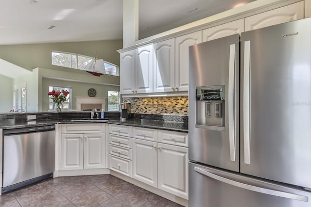 kitchen featuring dark stone counters, white cabinetry, appliances with stainless steel finishes, and lofted ceiling with skylight