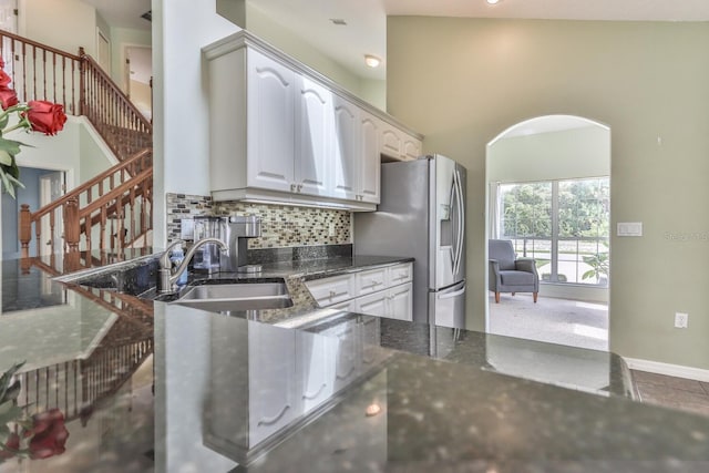 kitchen with tasteful backsplash, stainless steel fridge, white cabinets, dark stone countertops, and sink