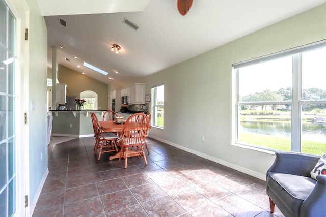 dining area featuring a water view, tile patterned floors, and lofted ceiling with skylight