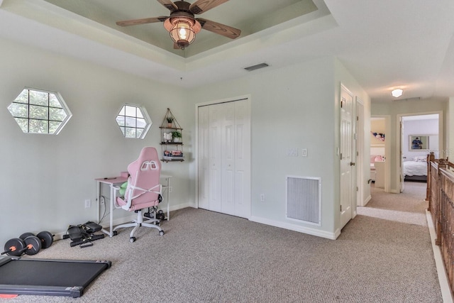 carpeted office space with ceiling fan and a raised ceiling