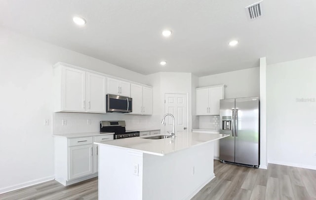 kitchen with white cabinets, appliances with stainless steel finishes, light wood-type flooring, and a kitchen island with sink