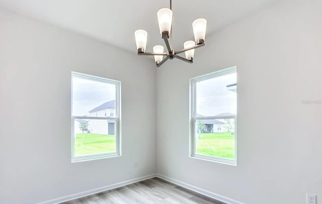 spare room with light wood-type flooring, an inviting chandelier, and a wealth of natural light