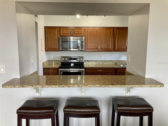 kitchen featuring light stone counters, stainless steel appliances, kitchen peninsula, and a kitchen breakfast bar