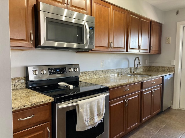 kitchen featuring appliances with stainless steel finishes, light stone countertops, sink, and dark tile patterned floors