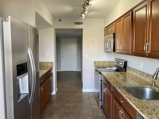 kitchen featuring dark tile patterned floors, light stone counters, sink, rail lighting, and stainless steel appliances