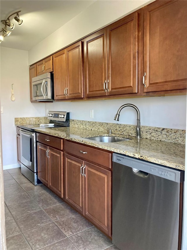 kitchen with light stone counters, stainless steel appliances, sink, and dark tile patterned flooring