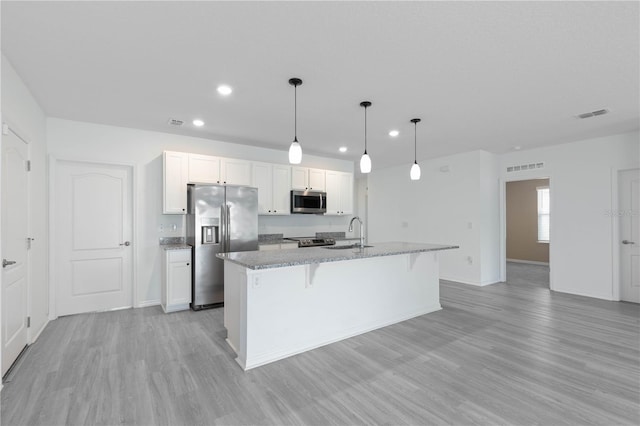 kitchen with white cabinets, light hardwood / wood-style flooring, a kitchen island with sink, pendant lighting, and appliances with stainless steel finishes