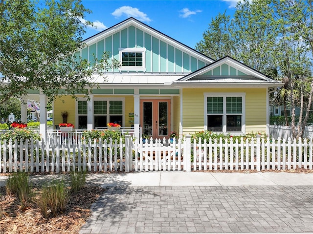 view of front of property with metal roof, a porch, a fenced front yard, board and batten siding, and a standing seam roof