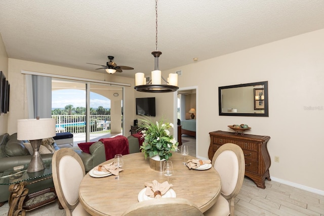 dining room with ceiling fan with notable chandelier, light wood-type flooring, and a textured ceiling