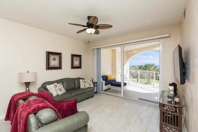 living room featuring a textured ceiling, light wood-type flooring, and ceiling fan