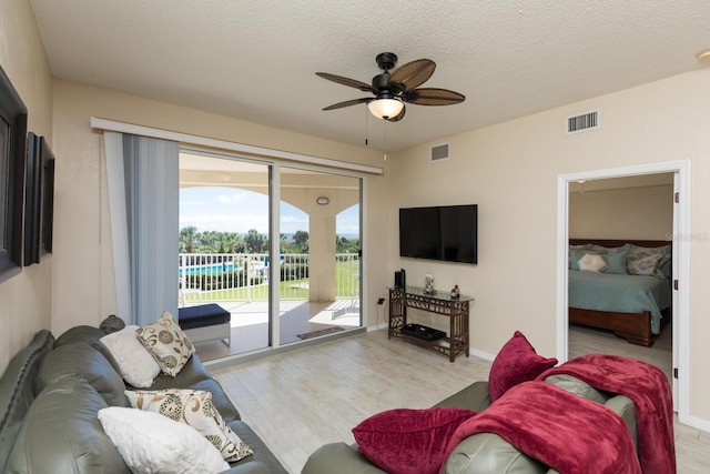 living room with ceiling fan, a textured ceiling, and light wood-type flooring