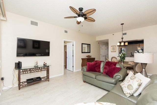 living room featuring light wood-type flooring, ceiling fan, and a textured ceiling