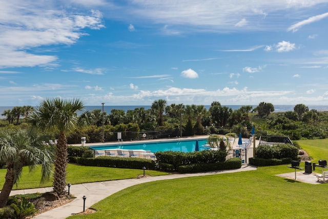 community pool with a water view, a yard, and fence