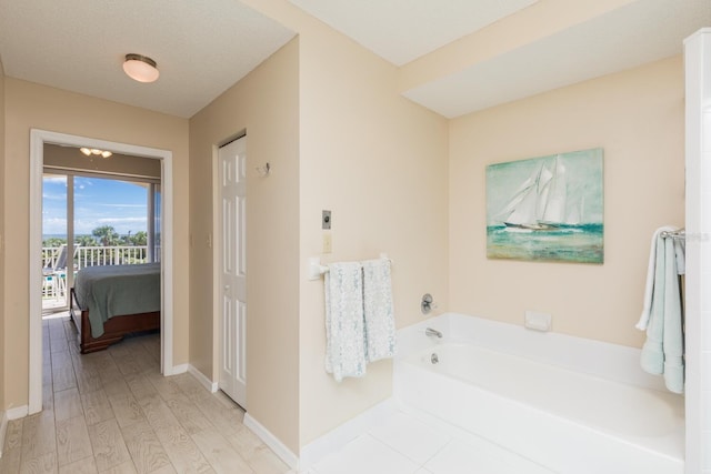 bathroom featuring ensuite bathroom, a textured ceiling, wood finished floors, baseboards, and a bath