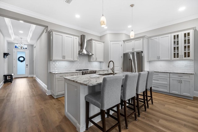 kitchen with stainless steel appliances, sink, wall chimney exhaust hood, a kitchen island with sink, and dark hardwood / wood-style flooring