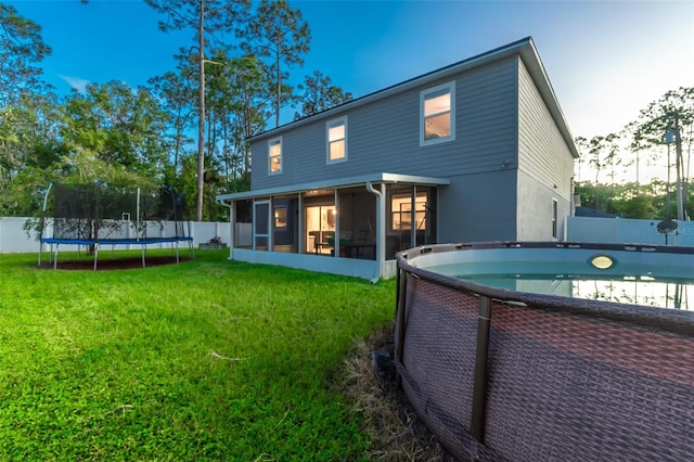 rear view of house with a sunroom, a fenced in pool, a trampoline, and a lawn