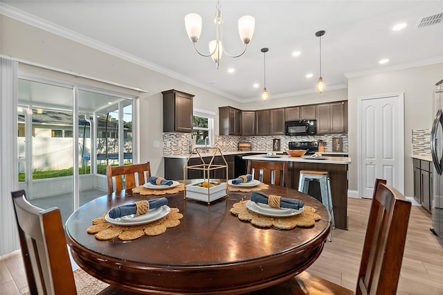 dining space featuring sink, ornamental molding, light hardwood / wood-style flooring, and an inviting chandelier