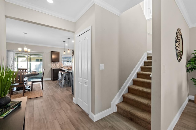 staircase with ornamental molding, wood-type flooring, and a notable chandelier