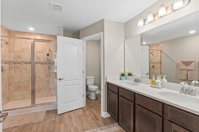 bathroom with hardwood / wood-style floors, vanity, toilet, and a shower with door