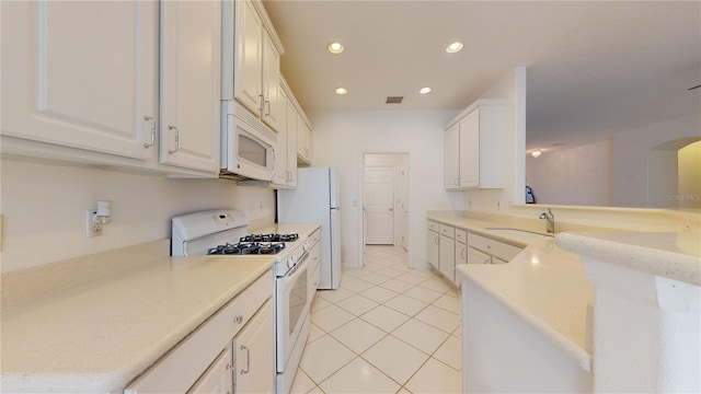 kitchen with sink, light tile patterned floors, kitchen peninsula, white appliances, and white cabinets