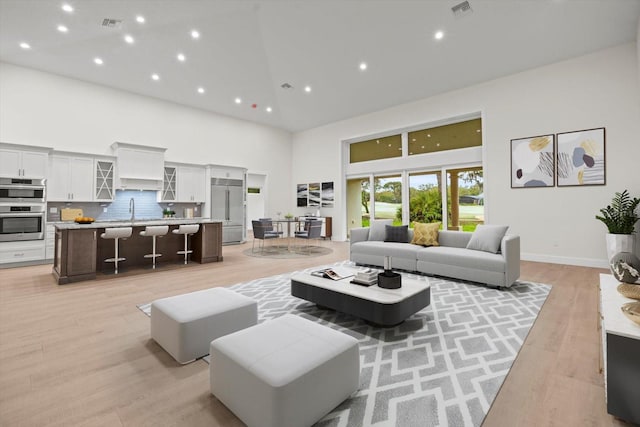 living room featuring sink, light hardwood / wood-style flooring, and high vaulted ceiling